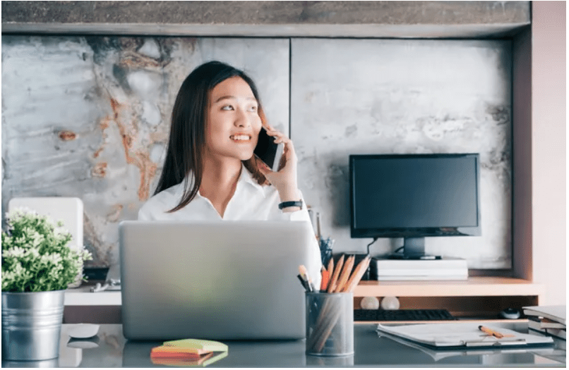 Woman smiling while talking on the phone at her desk with a laptop.