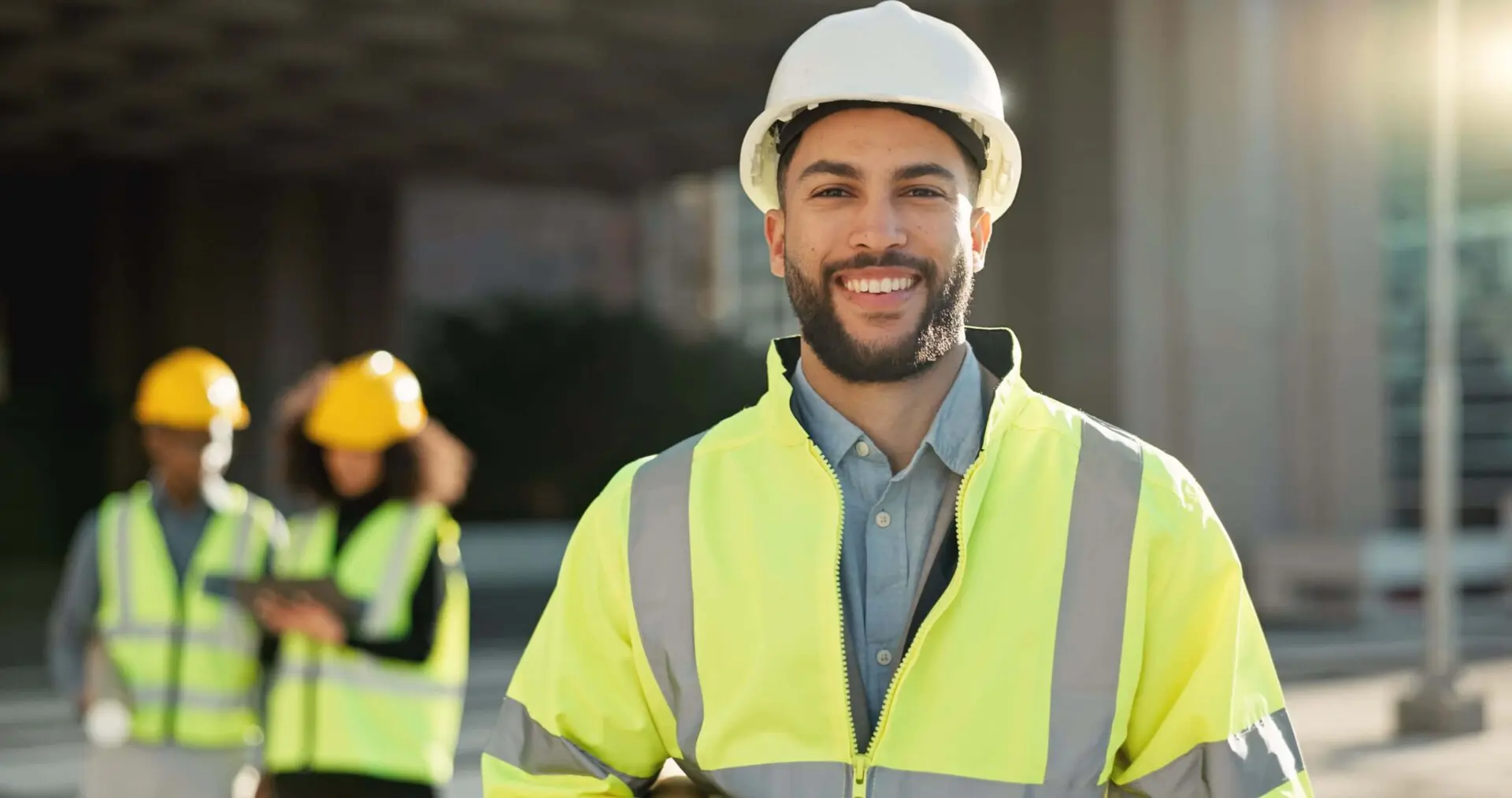 Smiling construction worker wearing a white helmet and yellow reflective vest.