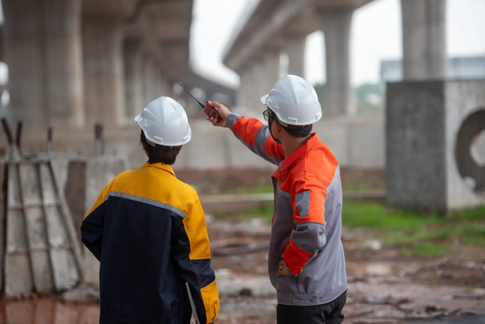 Two construction workers pointing toward elevated bridge